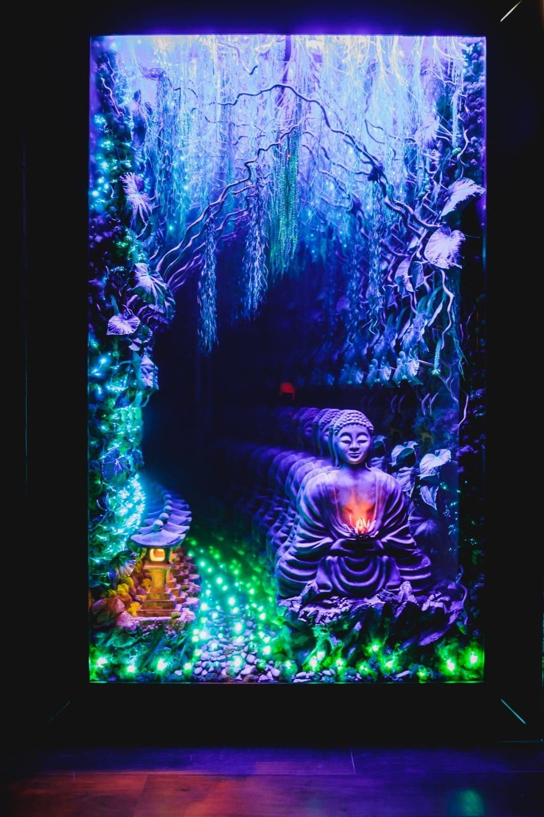 Blue and violet light surrounds a repeating Buddha sculpture in an infinity mirror.