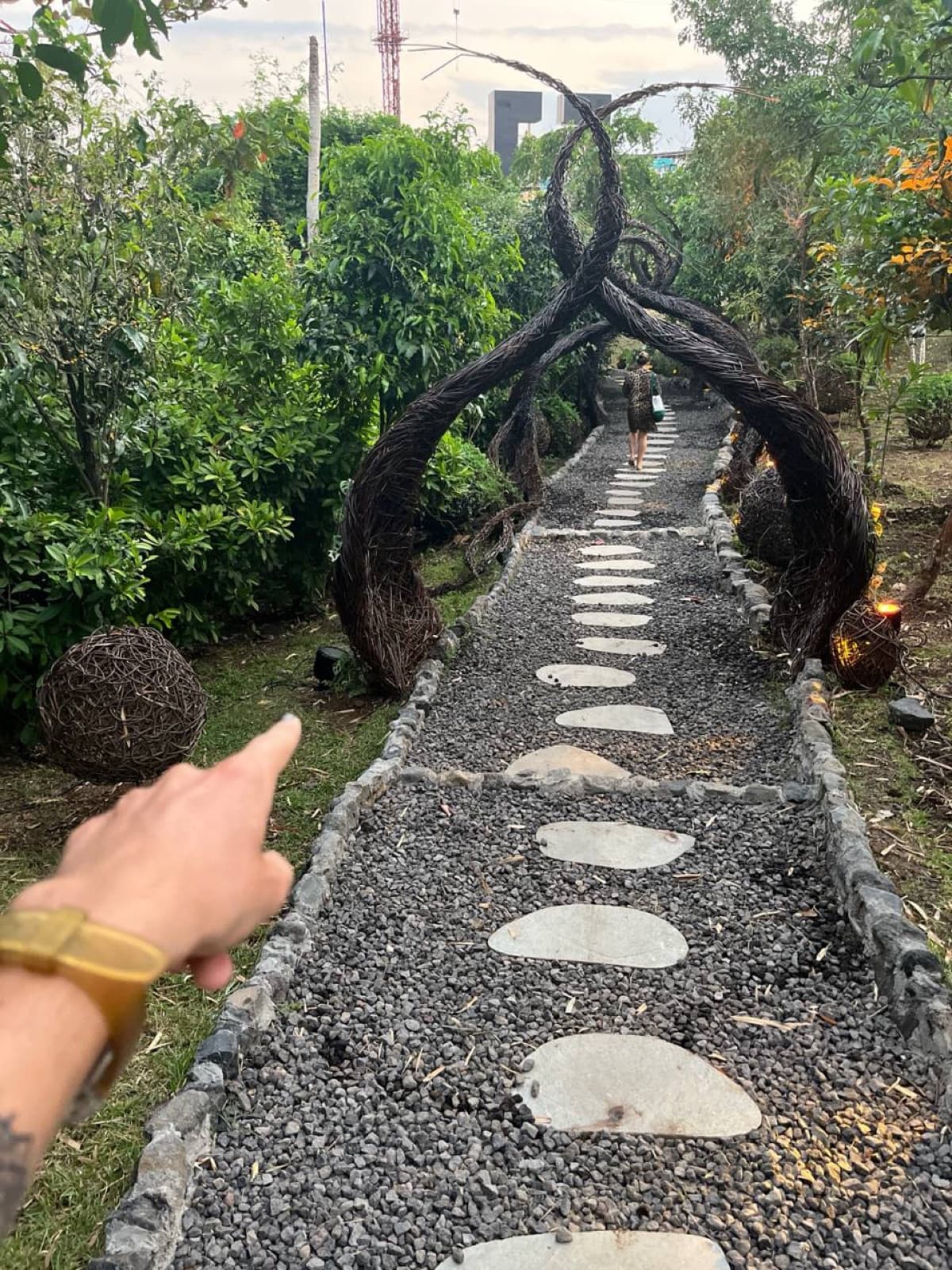 Aurora Park pathway with twisted black metal arches over stepping-stone path, woven sculpture in foreground.
