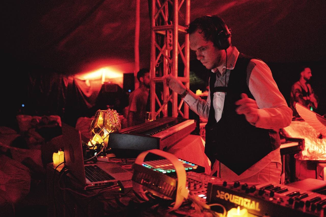 A live electronic performer working across keyboards and controllers in the red-lit booth