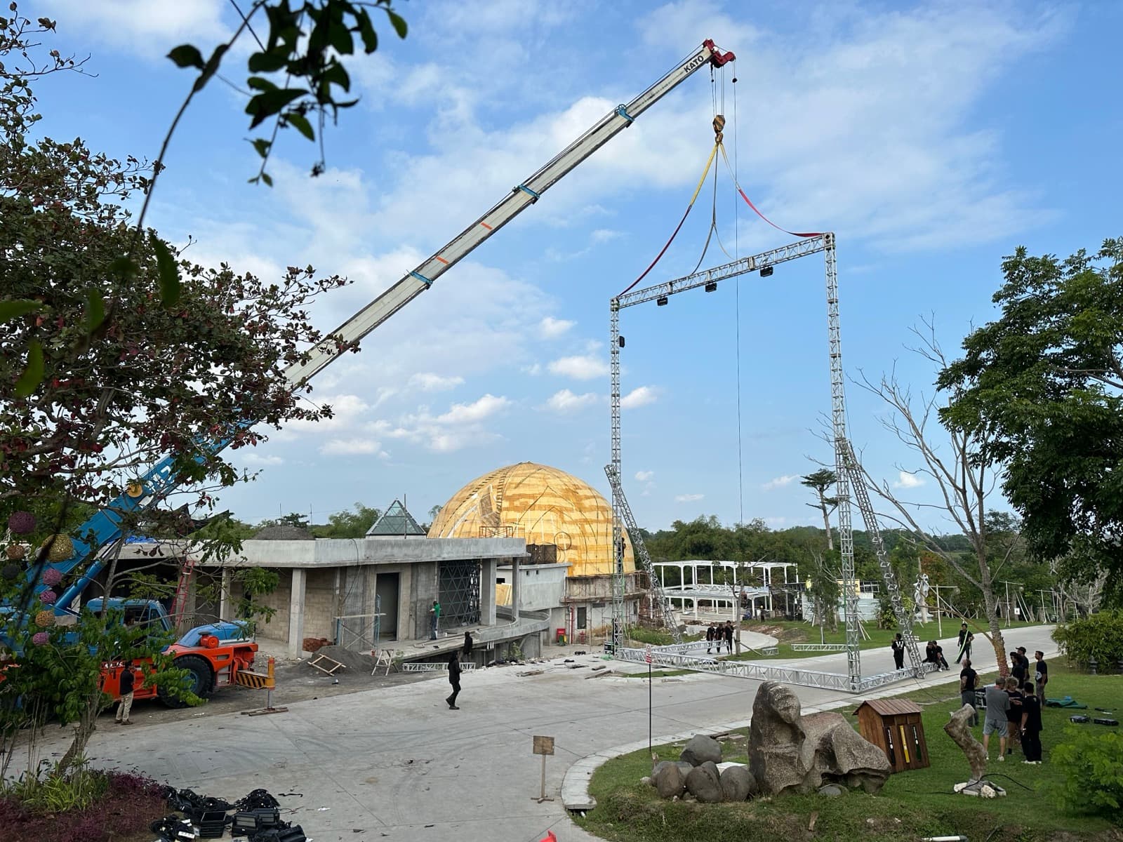 Install — a crane lifts the truss frame into position, golden dome of Nuanu's central pavilion visible behind.