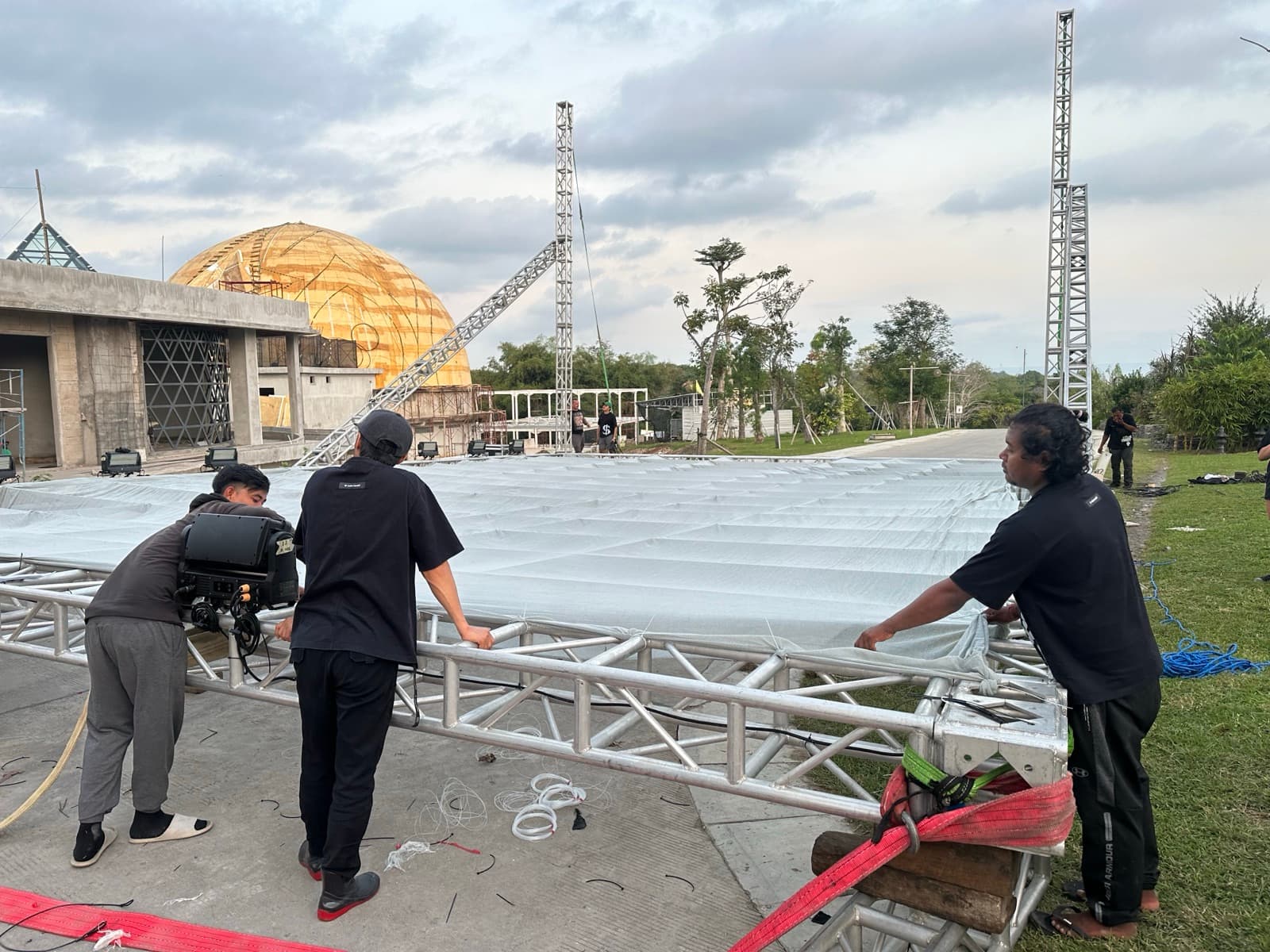 Install — three crew members tensioning the fabric across the horizontal beam, dome of Nuanu in the background.