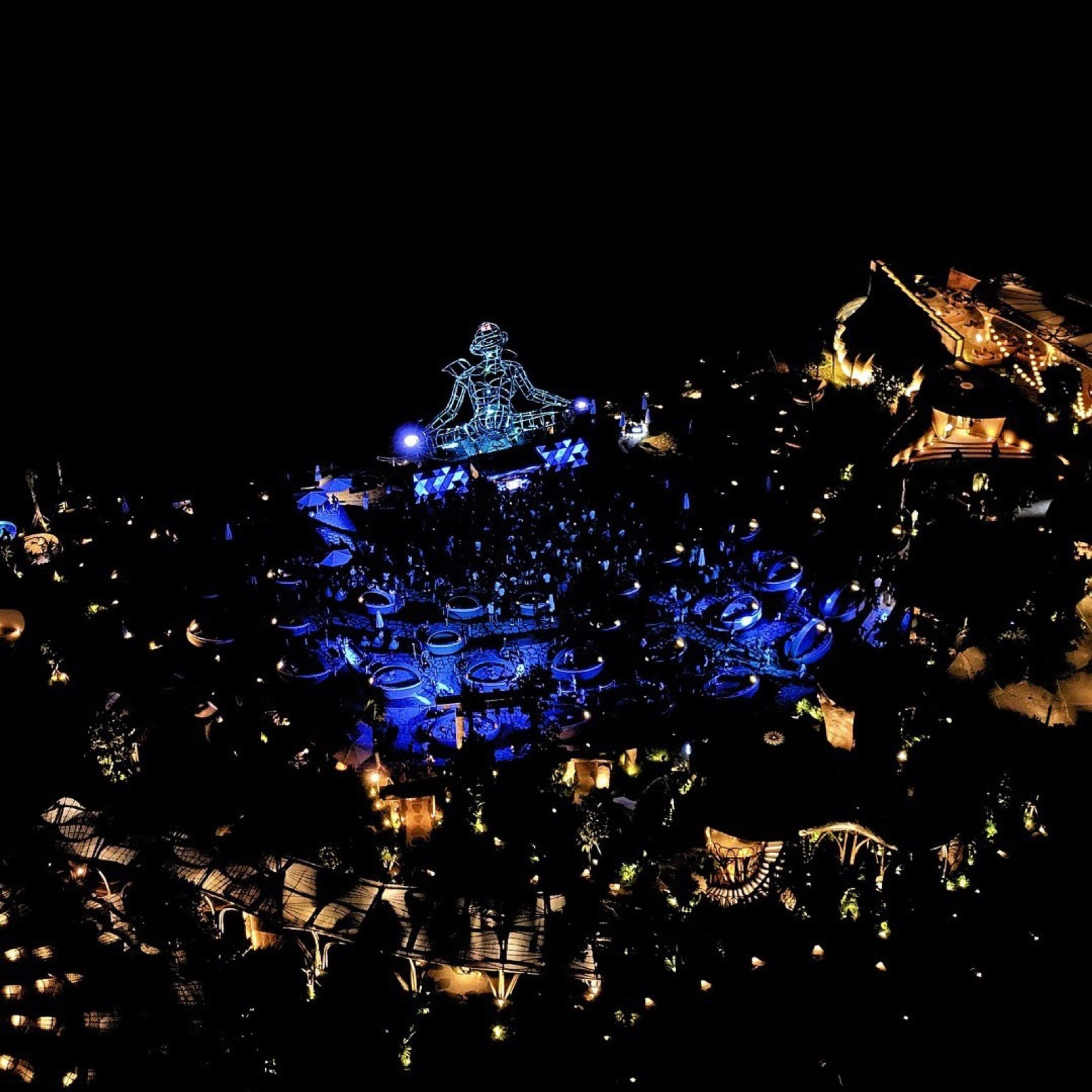 Aerial view of Luna Beach Club at night — LUNA sculpture lit blue at the centre of the venue.