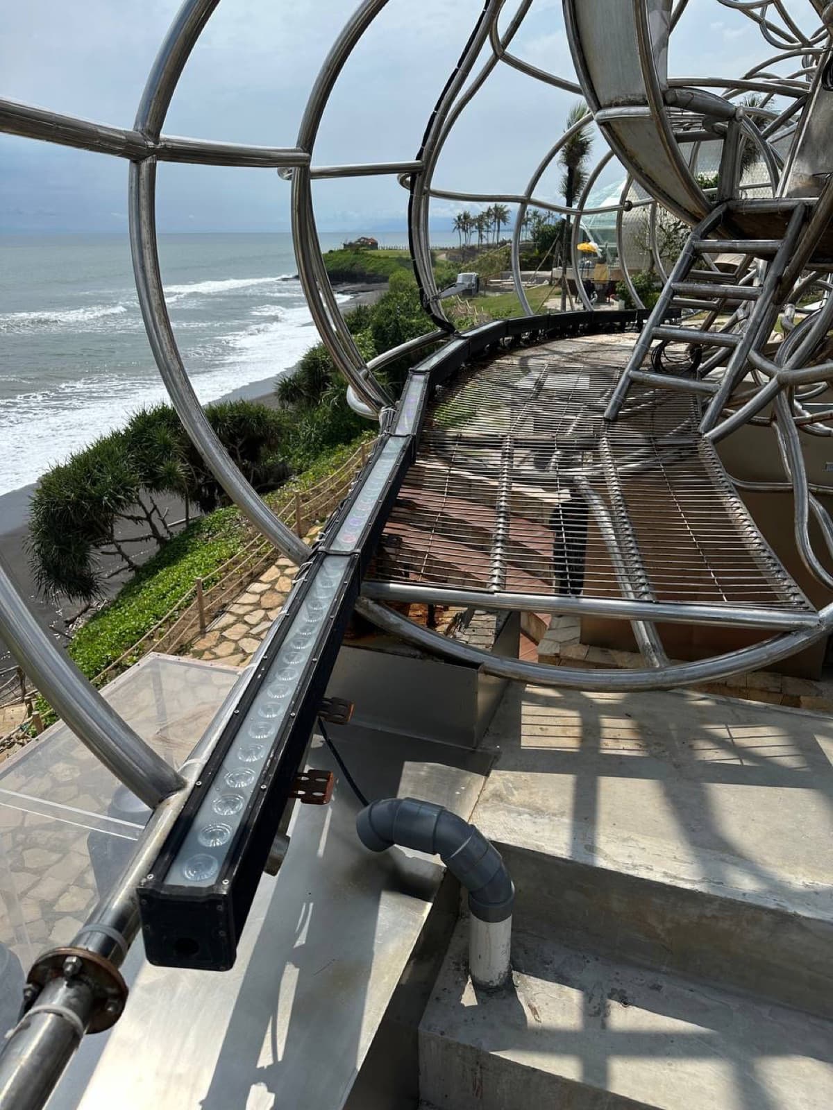 Looking outward from inside the LUNA sculpture — the wireframe steel forms a tunnel toward the beach and ocean horizon.