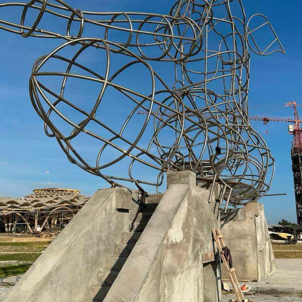 LUNA's wireframe sculpture mid-construction — steel armature rising from its concrete base, construction crane in the distance.