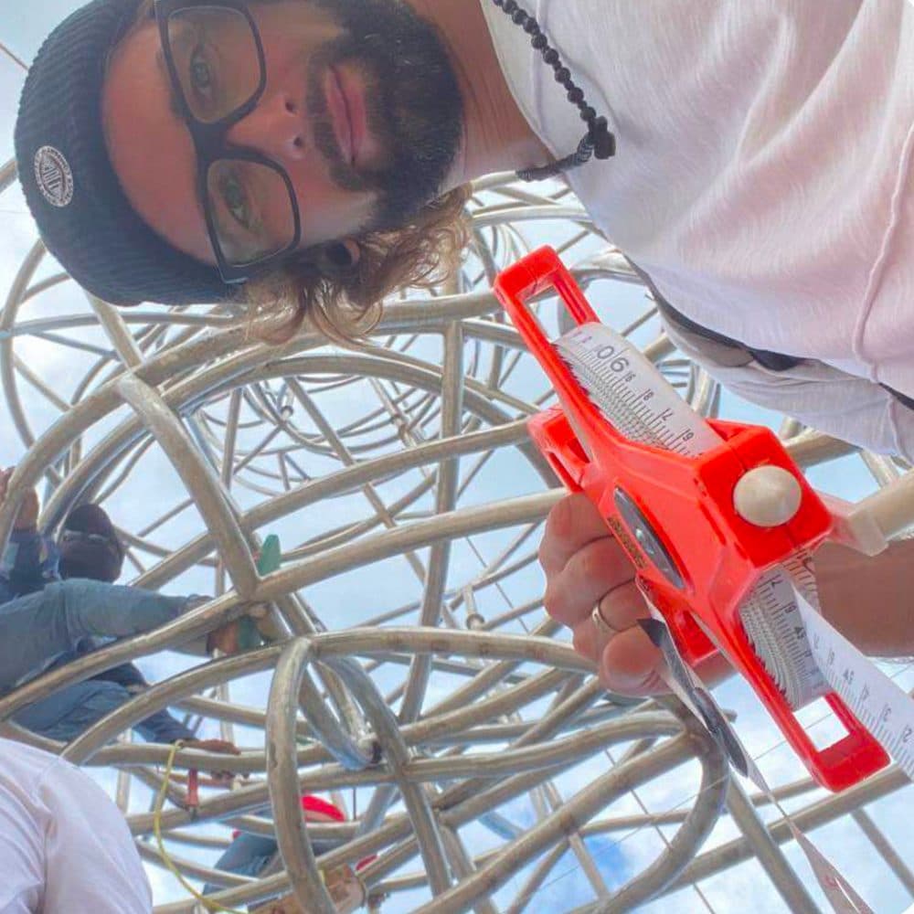 Inside LUNA — a builder grinning up at the camera from within the wireframe sphere, calibration tool in hand.