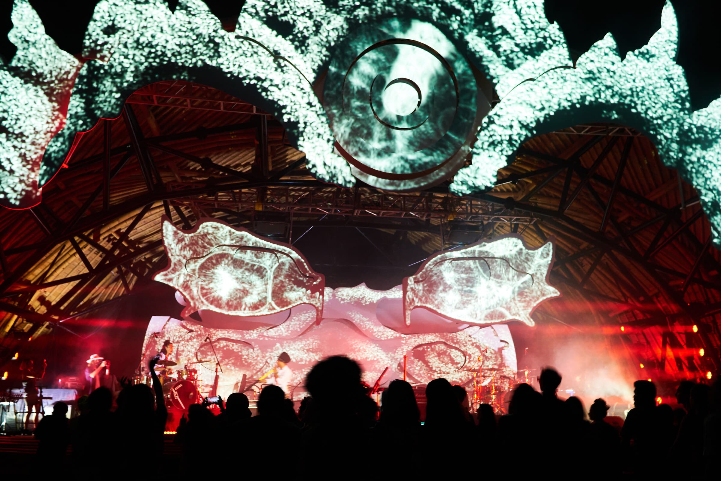 A live band performs beneath white and red projections on the Suara stage