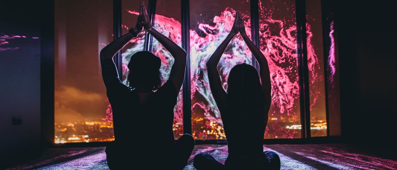 A resident gestures at the panoramic glass; pink and purple projection responds across the night cityscape.