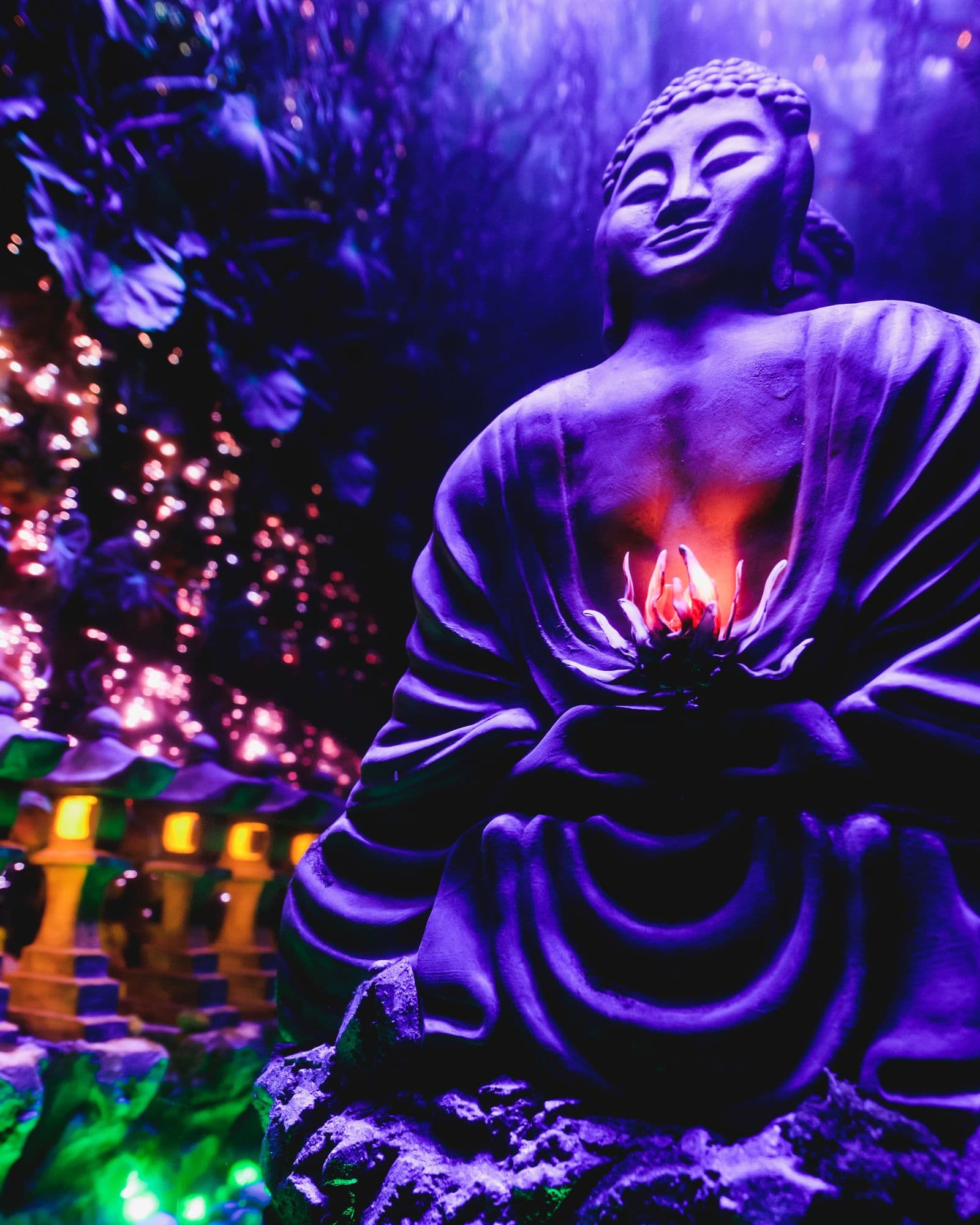 Sculpted Buddha figure holding a glowing lotus, surrounded by stone lanterns.