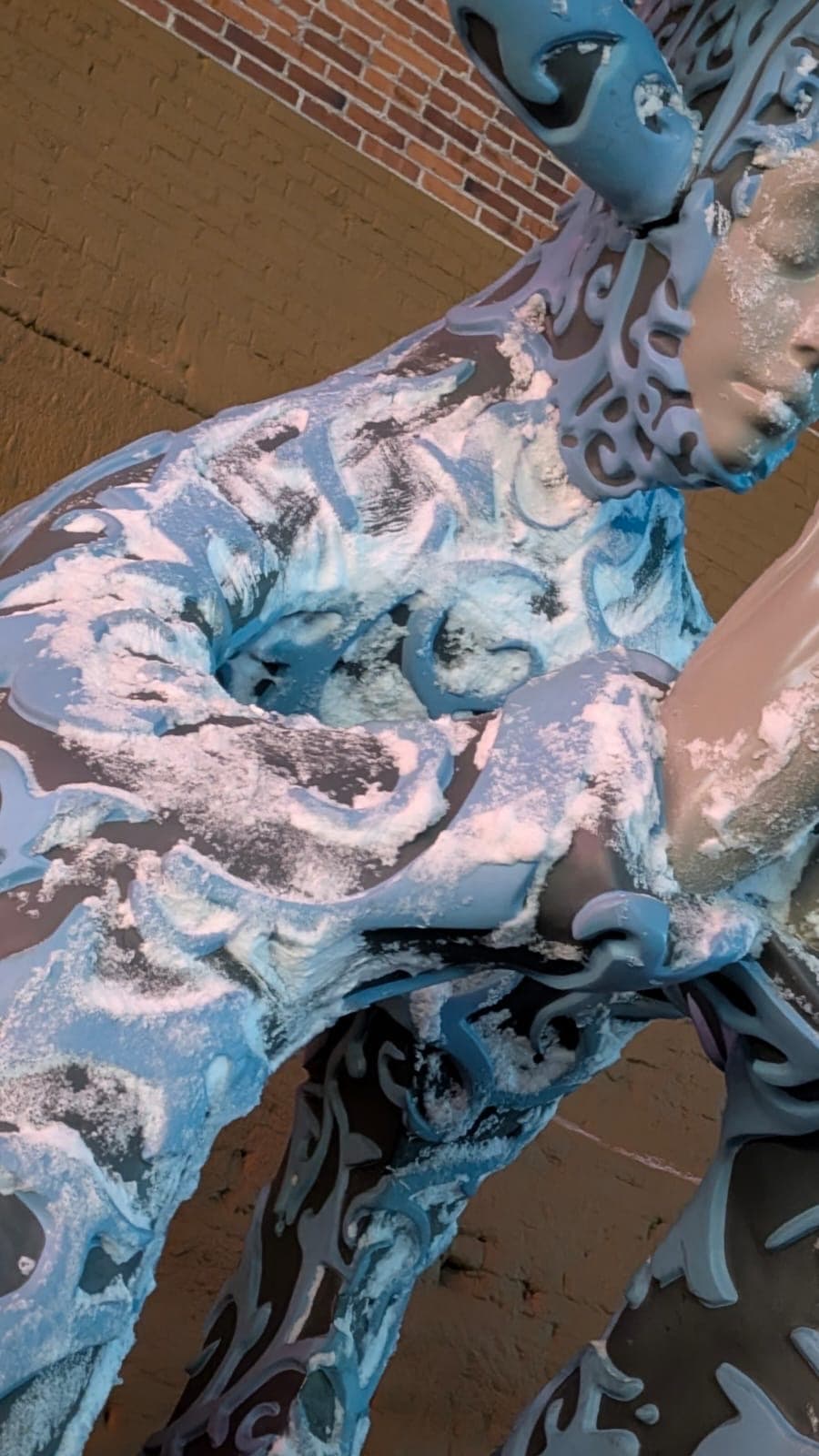 Close-up — the sculpture's ornate scrollwork covered in snow and ice, blue and silver tones picking up against the white.
