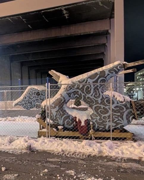 Install night — the sculpture's base under construction, surrounded by piles of snow, a forklift visible in the foreground, the parking-garage volume of downtown Reno behind.