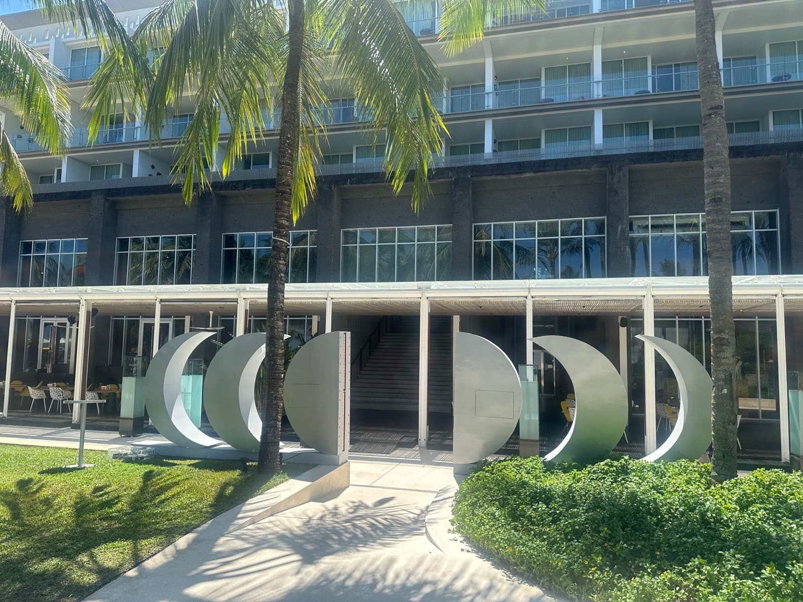 Daytime — five crescent sculptures arrayed in front of the hotel facade, palms framing the entrance.