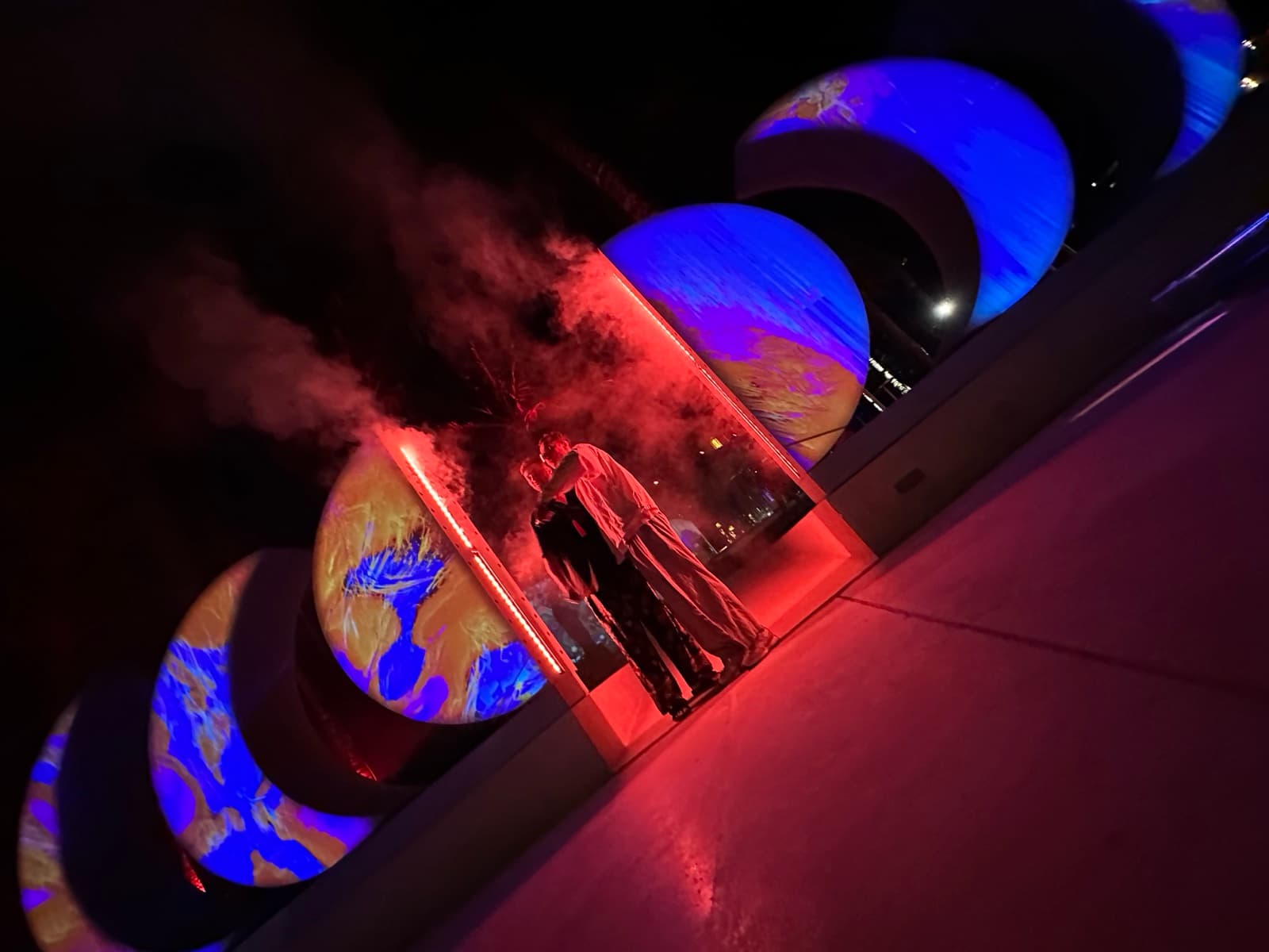 Nightfall — five crescents lit deep blue with projected texture, smoke drifting low across the platform, two silhouettes framed in the central crescent.